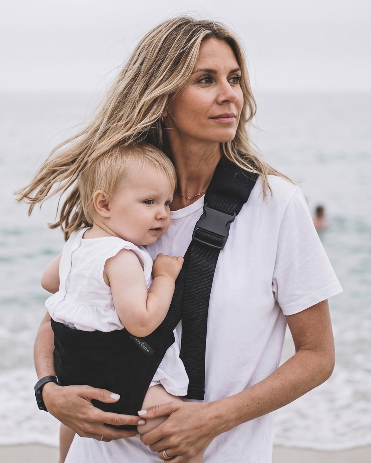 Mama na plaży niesie dziecko w czarnym nosidełku dla dzieci do 20 kg DereDere